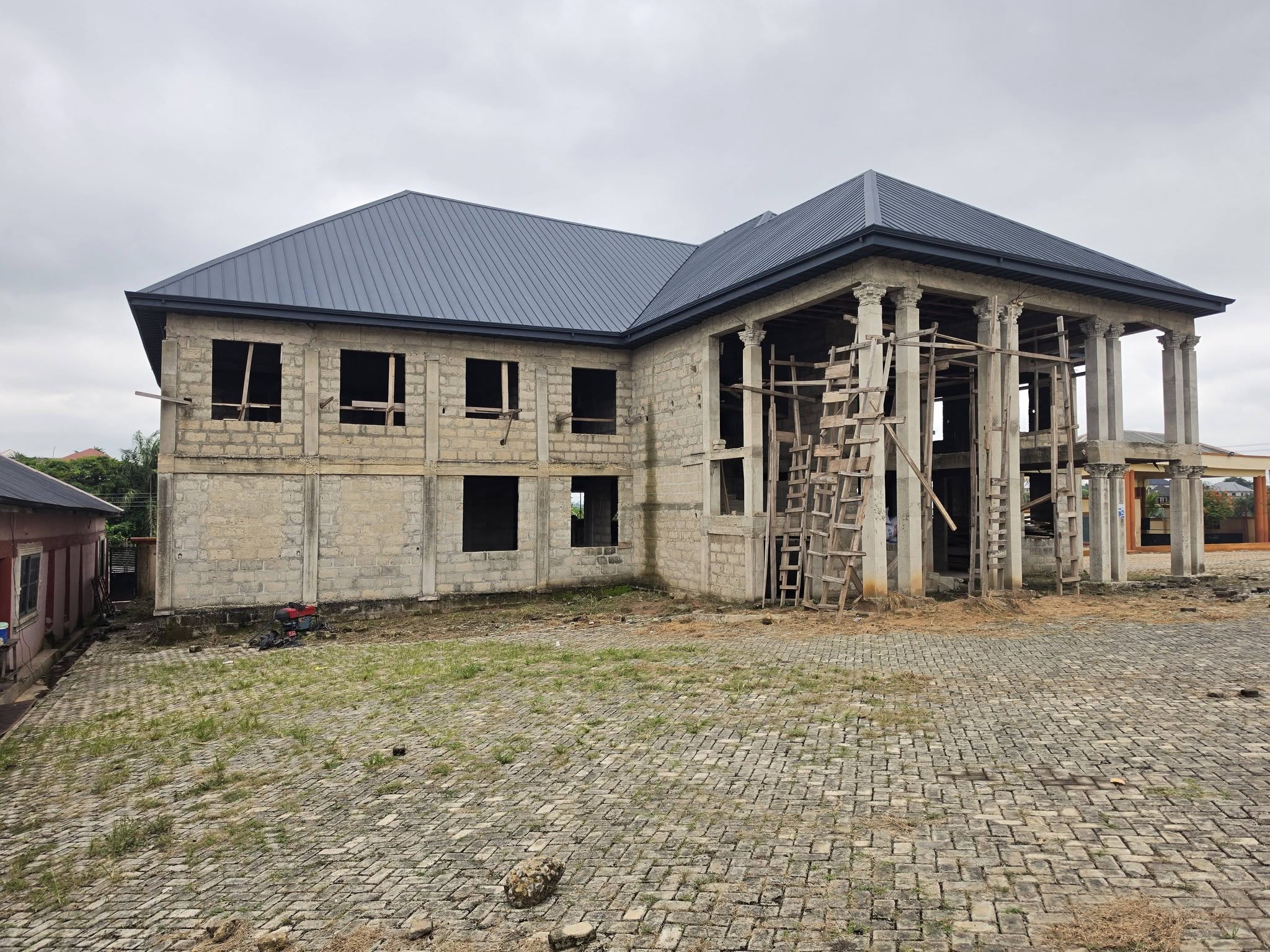 Grand two-storey residential villa under construction with classical decorative portico columns and durable dark roofing